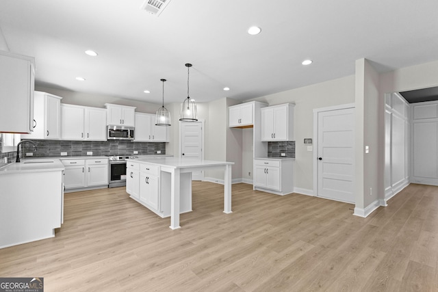 kitchen featuring white cabinetry, sink, pendant lighting, a kitchen island, and appliances with stainless steel finishes