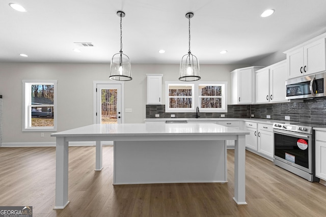 kitchen with a kitchen island, tasteful backsplash, decorative light fixtures, white cabinets, and appliances with stainless steel finishes