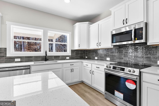 kitchen with light stone countertops, appliances with stainless steel finishes, white cabinetry, and sink