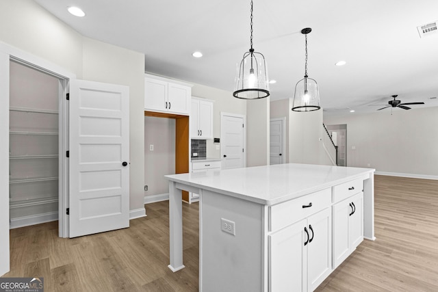 kitchen with pendant lighting, white cabinets, ceiling fan, light wood-type flooring, and a kitchen island