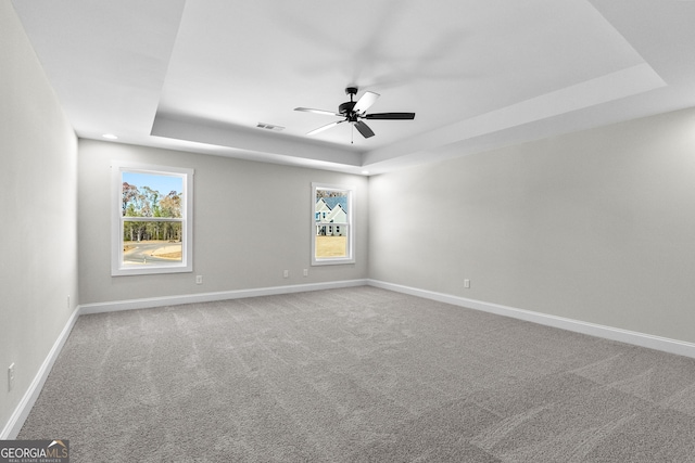 empty room featuring carpet, a raised ceiling, and ceiling fan