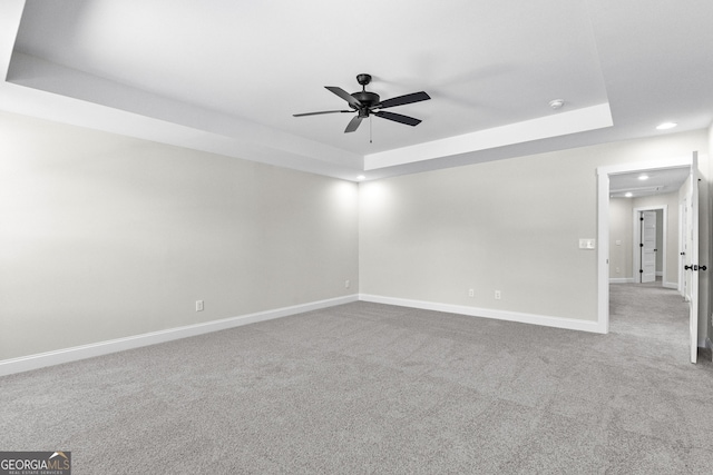 empty room with ceiling fan, carpet floors, and a tray ceiling