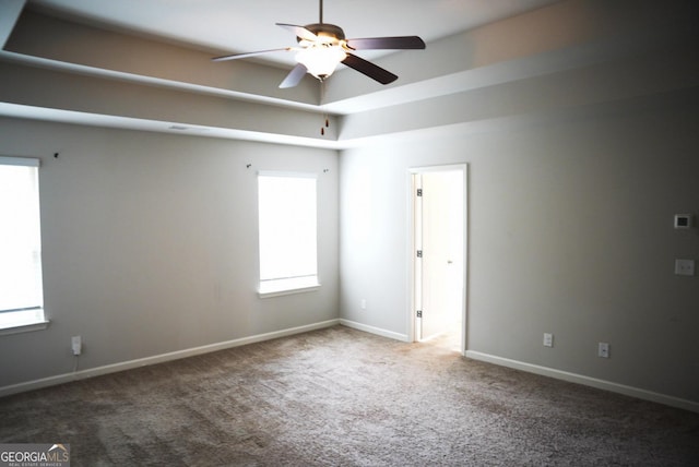 carpeted empty room featuring a raised ceiling, baseboards, and ceiling fan