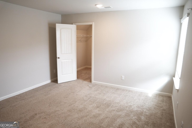 unfurnished bedroom with a spacious closet, a closet, baseboards, and carpet