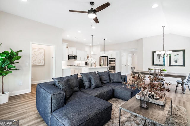 living room with ceiling fan with notable chandelier, light hardwood / wood-style flooring, and vaulted ceiling