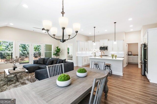 dining area featuring light hardwood / wood-style floors, vaulted ceiling, and an inviting chandelier