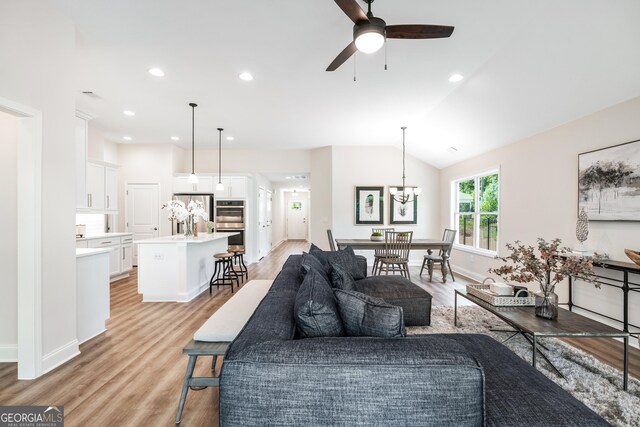 living room featuring lofted ceiling, light hardwood / wood-style flooring, and ceiling fan with notable chandelier