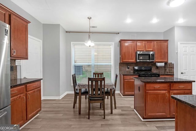 kitchen featuring appliances with stainless steel finishes, light wood-type flooring, dark stone countertops, a kitchen island, and hanging light fixtures