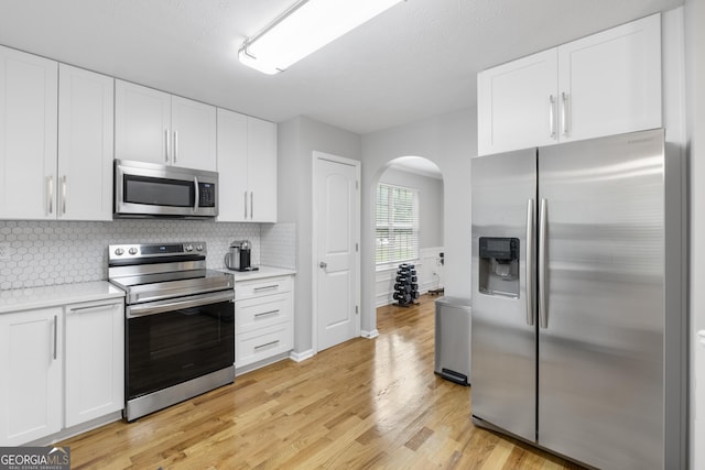 kitchen featuring backsplash, white cabinets, light wood-type flooring, and appliances with stainless steel finishes