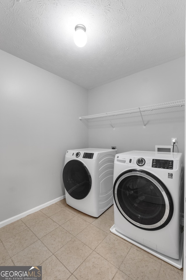 clothes washing area with independent washer and dryer, a textured ceiling, and light tile patterned floors