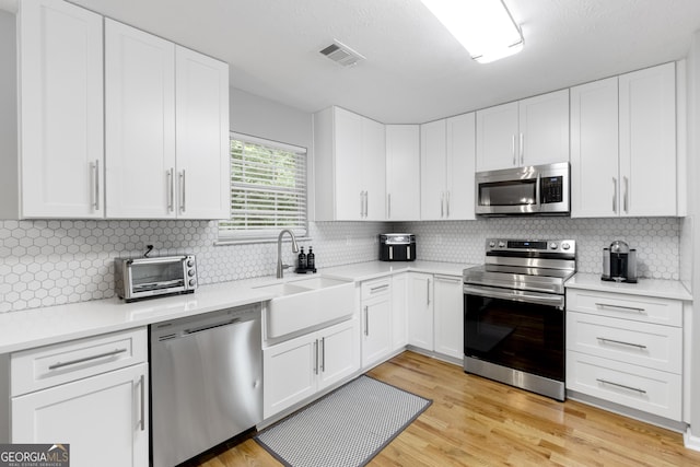 kitchen featuring backsplash, sink, light wood-type flooring, appliances with stainless steel finishes, and white cabinetry