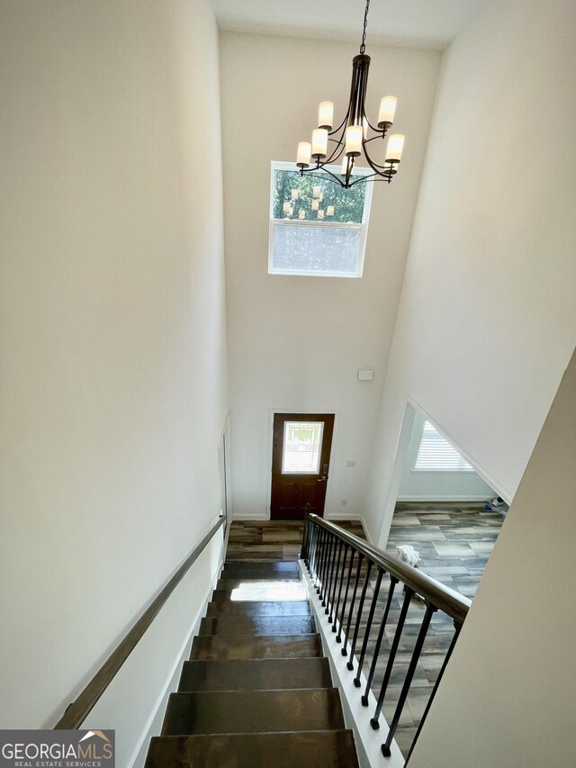 stairs featuring hardwood / wood-style flooring, a towering ceiling, and a chandelier