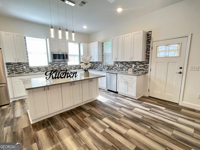 kitchen with a center island, decorative light fixtures, light stone counters, white cabinetry, and stainless steel appliances