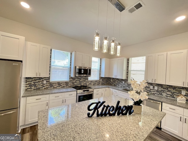 kitchen with white cabinetry, pendant lighting, light stone counters, and appliances with stainless steel finishes