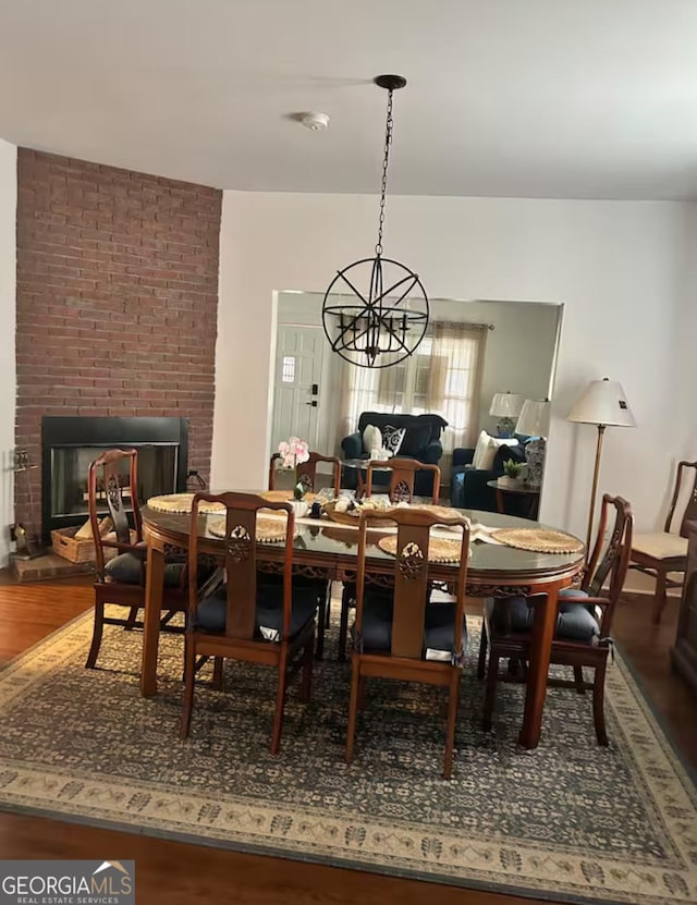 dining area featuring hardwood / wood-style flooring, a notable chandelier, and a brick fireplace