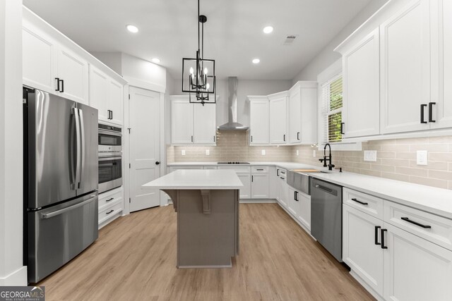 kitchen with a center island, sink, stainless steel appliances, wall chimney range hood, and white cabinets