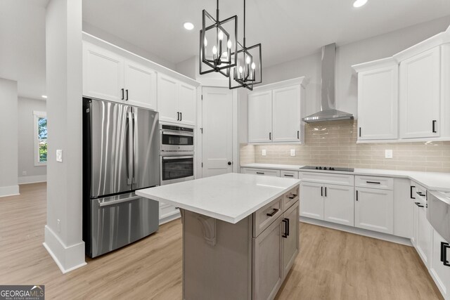 kitchen featuring appliances with stainless steel finishes, wall chimney range hood, white cabinets, a center island, and light hardwood / wood-style floors