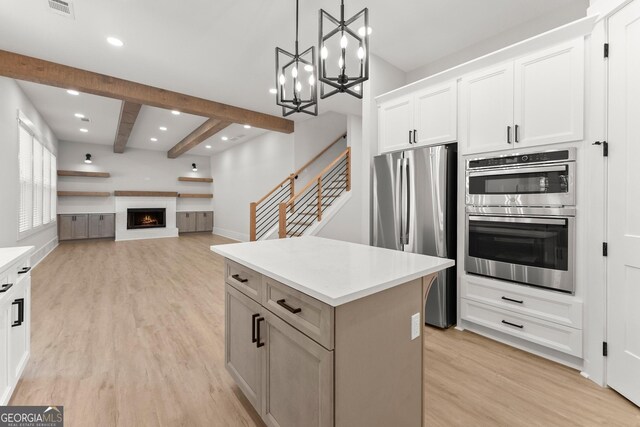 kitchen with appliances with stainless steel finishes, pendant lighting, white cabinets, light hardwood / wood-style floors, and a kitchen island