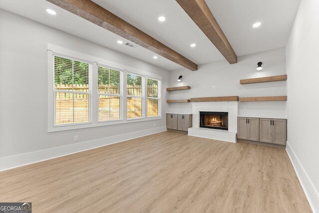 unfurnished living room featuring a fireplace, beamed ceiling, and light wood-type flooring