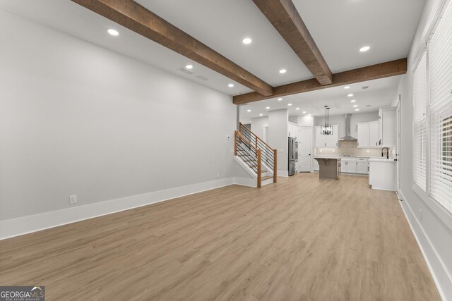 unfurnished living room featuring light hardwood / wood-style flooring, beamed ceiling, a notable chandelier, and sink