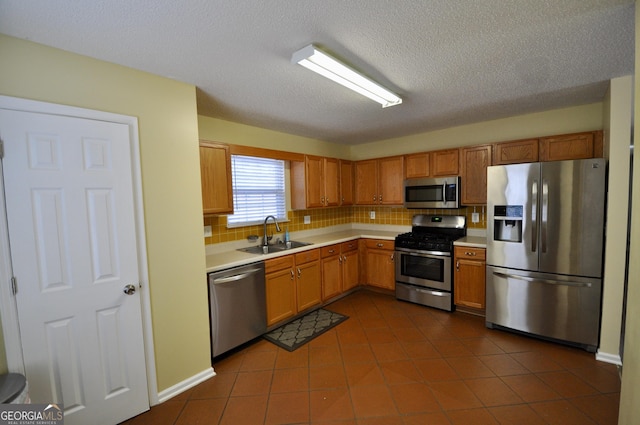 kitchen with appliances with stainless steel finishes, tasteful backsplash, a textured ceiling, dark tile patterned floors, and sink