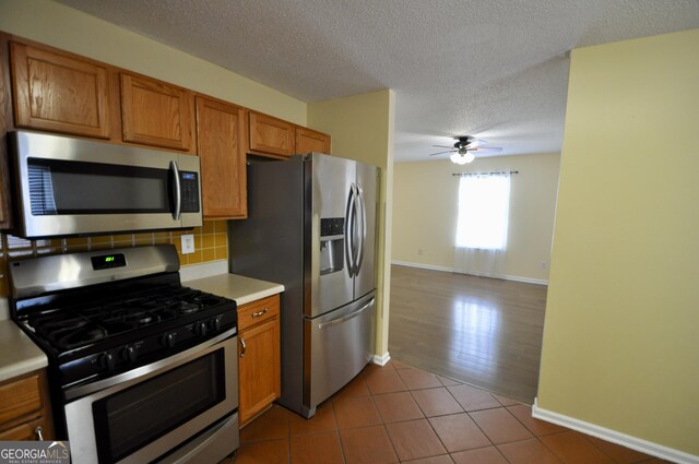 kitchen with ceiling fan, stainless steel appliances, a textured ceiling, decorative backsplash, and light tile patterned floors