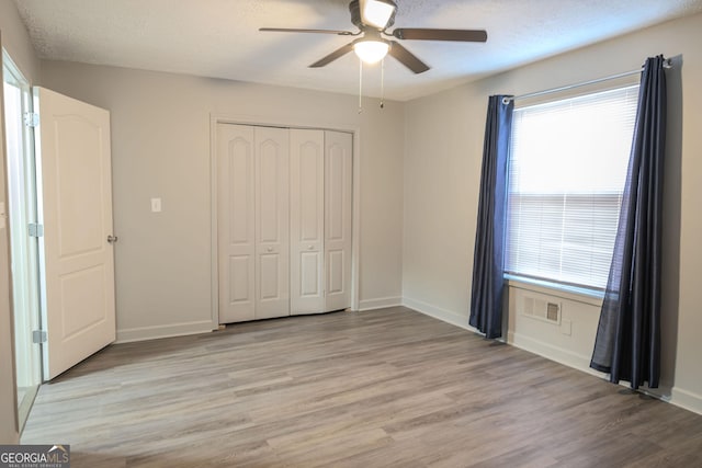 unfurnished bedroom featuring multiple windows, ceiling fan, a closet, and light hardwood / wood-style floors