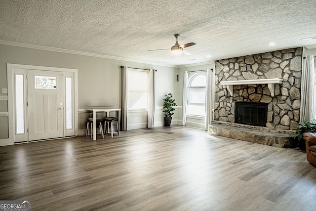 unfurnished living room with a textured ceiling, a stone fireplace, ceiling fan, and a healthy amount of sunlight