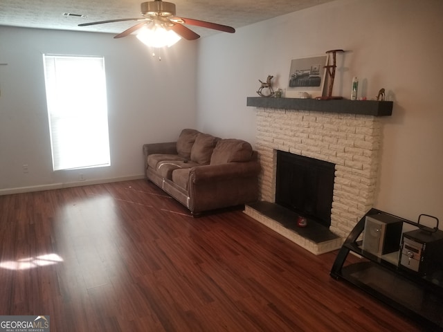 living room featuring ceiling fan, dark wood-type flooring, a textured ceiling, and a brick fireplace