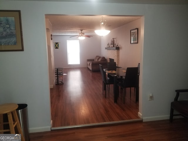 dining space featuring wood finished floors, a ceiling fan, baseboards, and a brick fireplace
