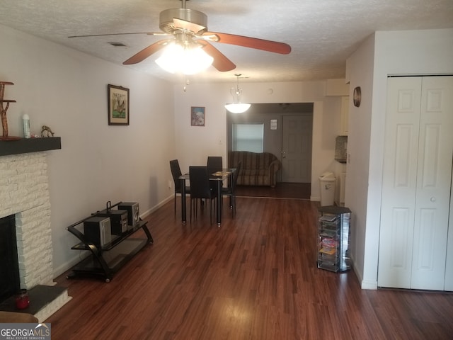 dining space featuring a fireplace, a textured ceiling, ceiling fan, and dark wood-type flooring