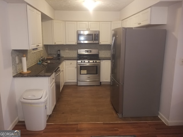 kitchen with appliances with stainless steel finishes, dark wood-style flooring, white cabinetry, and decorative backsplash