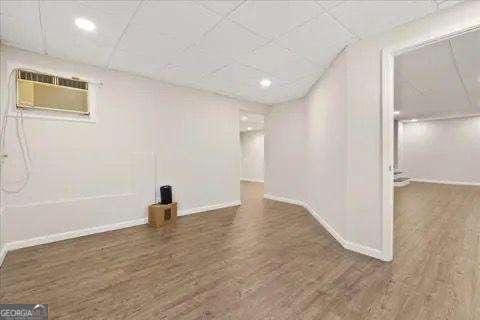 basement with a paneled ceiling, dark hardwood / wood-style floors, and an AC wall unit