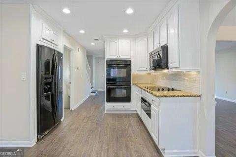 kitchen featuring black appliances, decorative backsplash, white cabinetry, and hardwood / wood-style floors