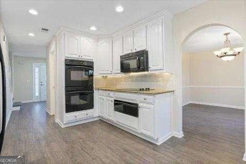 kitchen featuring white cabinets, tasteful backsplash, black appliances, and dark wood-type flooring