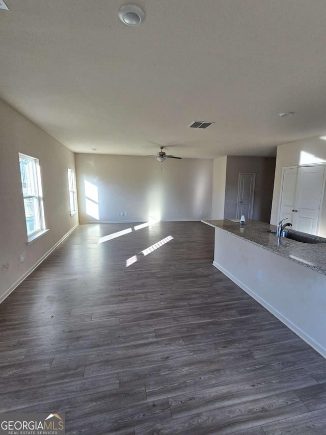 unfurnished living room featuring ceiling fan, sink, and dark wood-type flooring