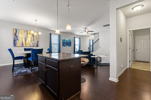 kitchen with ceiling fan with notable chandelier, dark hardwood / wood-style floors, decorative light fixtures, a kitchen island, and a kitchen bar