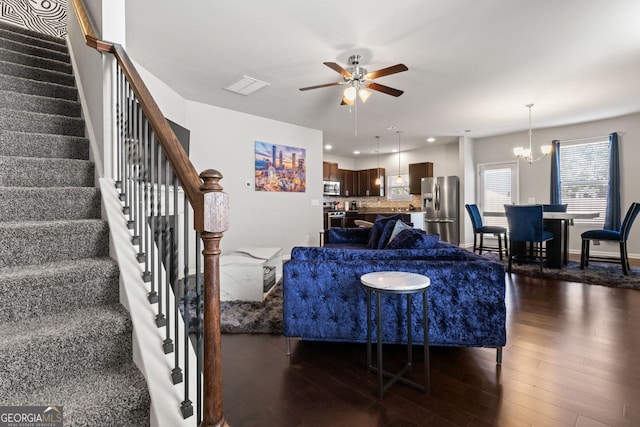 living room with ceiling fan with notable chandelier and dark hardwood / wood-style flooring