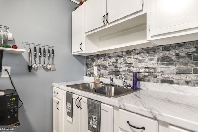 kitchen with decorative backsplash, white cabinetry, sink, and light stone countertops