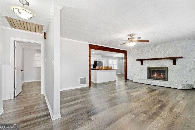 unfurnished living room with a fireplace, wood-type flooring, ceiling fan, and ornamental molding