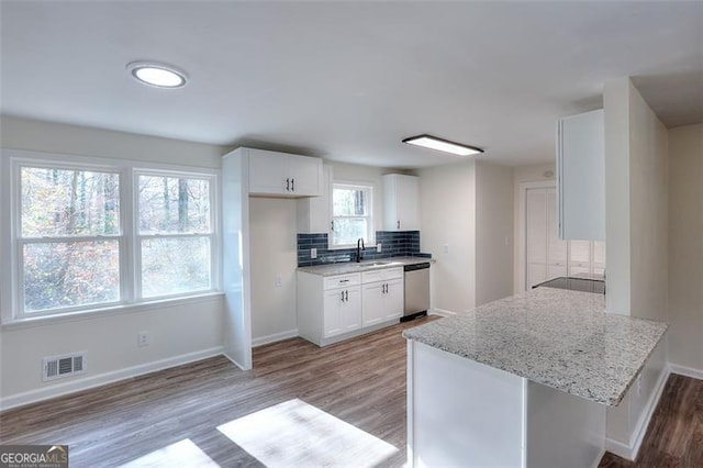 kitchen featuring white cabinetry, dishwasher, light stone countertops, backsplash, and kitchen peninsula