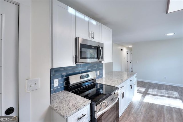 kitchen featuring light hardwood / wood-style flooring, decorative backsplash, appliances with stainless steel finishes, light stone counters, and white cabinetry