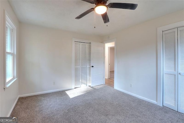 unfurnished bedroom featuring carpet, ceiling fan, and two closets