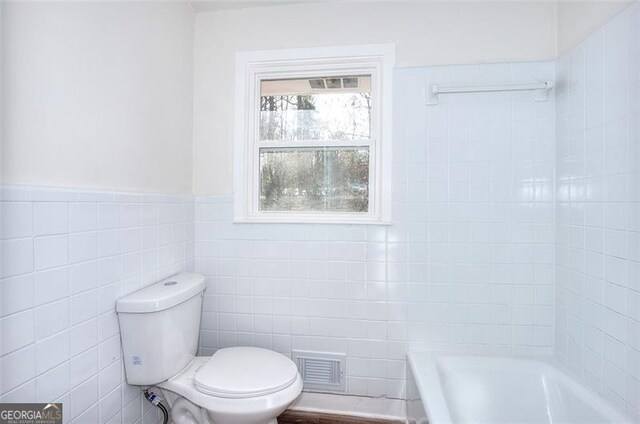 bathroom featuring a bathtub, toilet, and tile walls