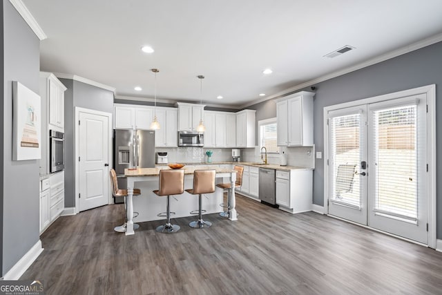 kitchen with white cabinets, hanging light fixtures, a kitchen island, a kitchen bar, and stainless steel appliances