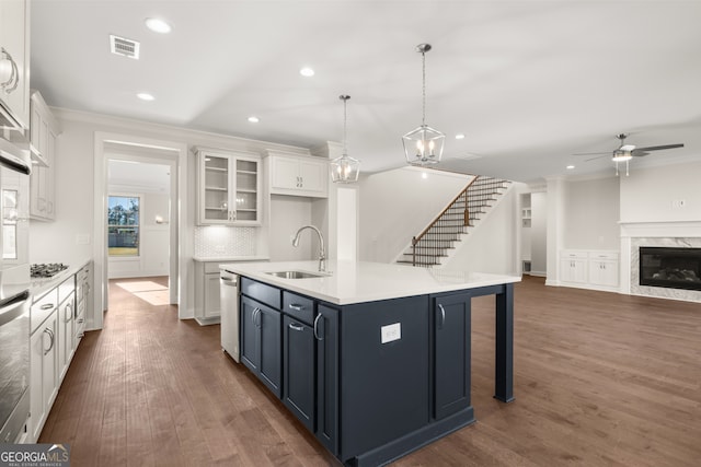 kitchen featuring sink, white cabinetry, hanging light fixtures, a fireplace, and a kitchen island with sink