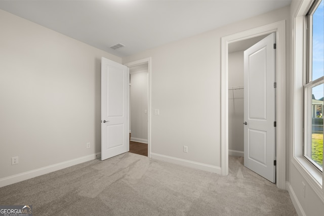 unfurnished bedroom with a spacious closet, light carpet, and a closet