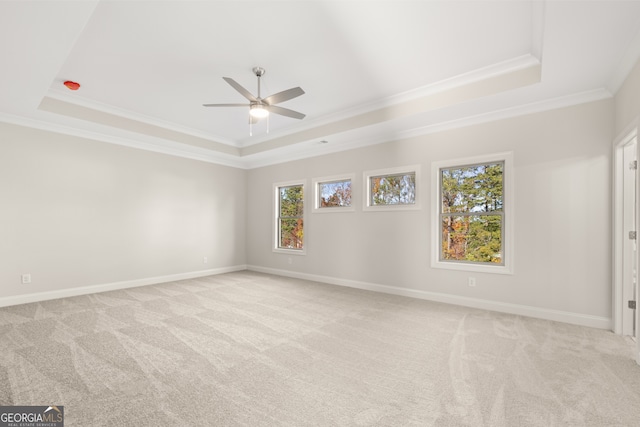 empty room with crown molding, a tray ceiling, light colored carpet, and ceiling fan