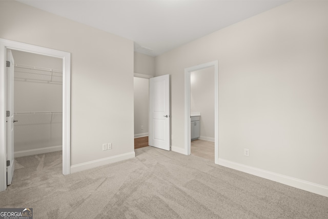 unfurnished bedroom featuring connected bathroom, a spacious closet, light carpet, and a closet