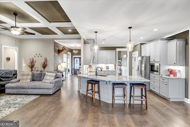 kitchen featuring light stone countertops, sink, coffered ceiling, pendant lighting, and a kitchen bar